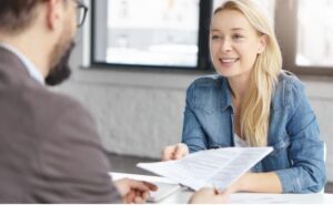 Une femme souriante présente son CV à un recruteur lors d'un entretien d'embauche.