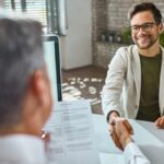 Deux personnes se serrent la main à travers un bureau, l'une d'elles tenant un CV.