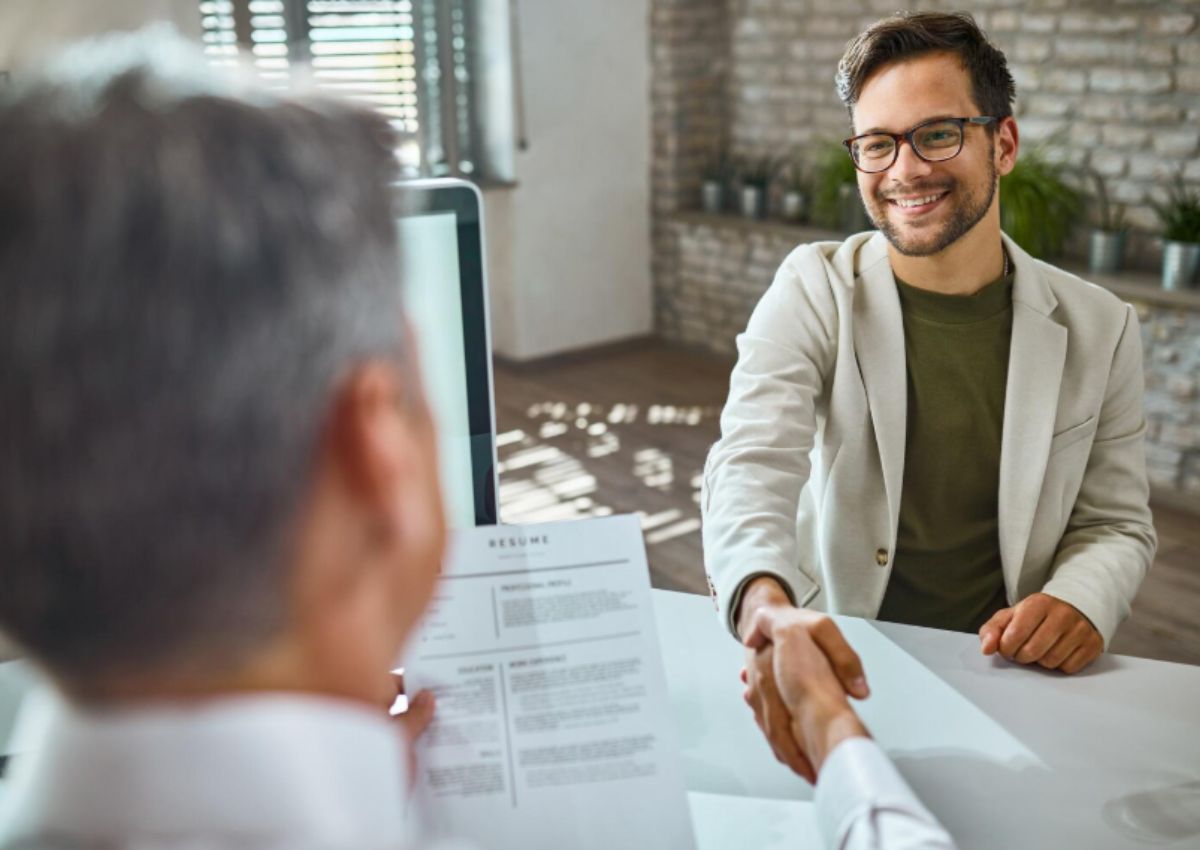 Deux personnes se serrent la main à travers un bureau, l'une d'elles tenant un CV.