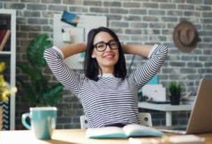 a woman sitting at a desk with her hands behind her head
