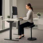 Illustration d’un tabouret ergonomique moderne utilisé à un poste informatique. L’image met en avant la posture active, la stabilité et le confort d’un espace de travail haut de gamme.