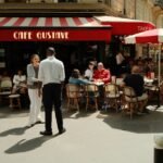 People sitting at tables outside Cafe Gustave on a sunny sidewalk in Paris