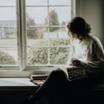A woman in a white sweater holding a mug while reading a book