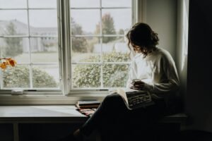 A woman in a white sweater holding a mug while reading a book