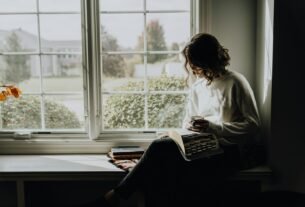 A woman in a white sweater holding a mug while reading a book