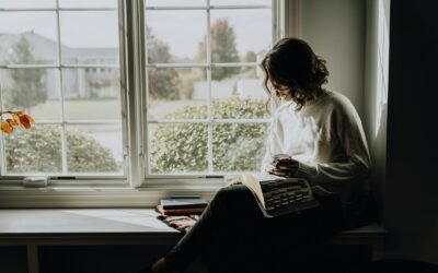 A woman in a white sweater holding a mug while reading a book